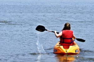 Person kayaking on a calm blue lake wearing a red life jacket.