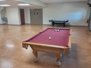 A pool table with burgundy felt and an air hockey table in a spacious room.