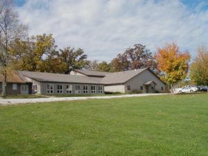 A large house with a gray roof surrounded by autumn trees and a green lawn.