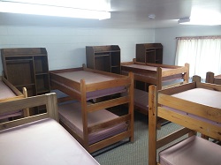 A dormitory room with multiple wooden bunk beds arranged neatly.