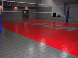 Indoor volleyball court with red and gray flooring and net.