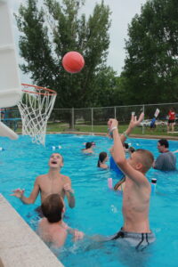 Kids playing basketball in a pool, jumping to score a basket.