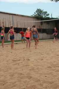 Young girls playing volleyball on a sandy court outdoors.