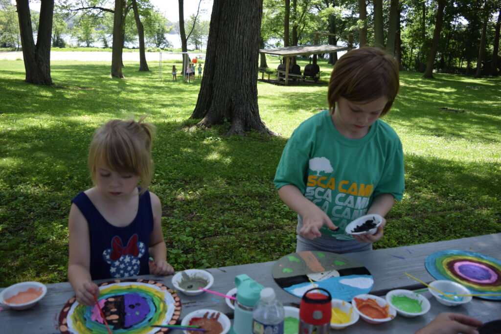 Two children painting outdoors at a park picnic table.