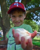 A smiling boy in a red cap offers ice cream to the camera.