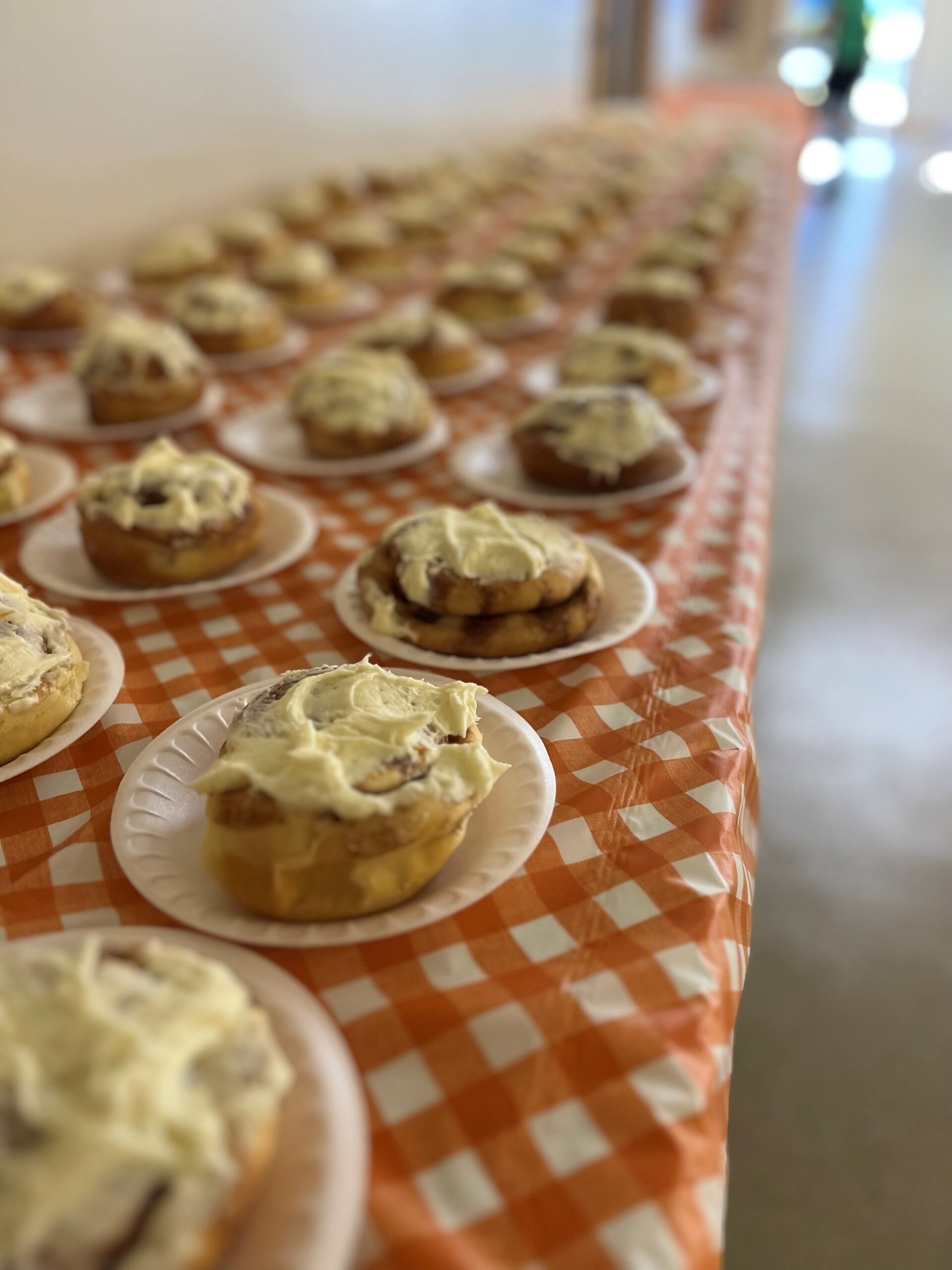Rows of frosted cinnamon rolls on a checkered tablecloth.