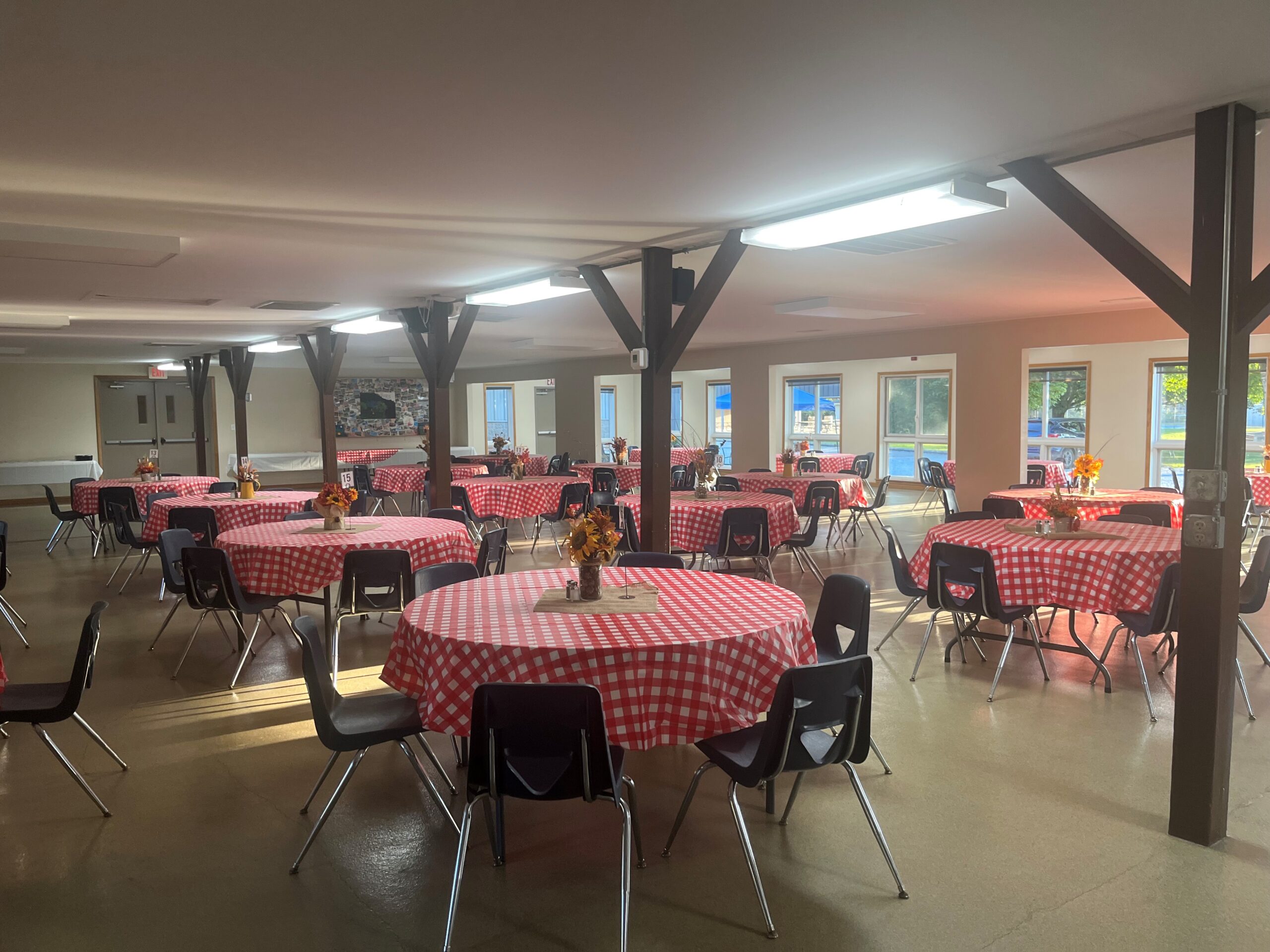 Room with round tables covered in red checkered tablecloths and black chairs.