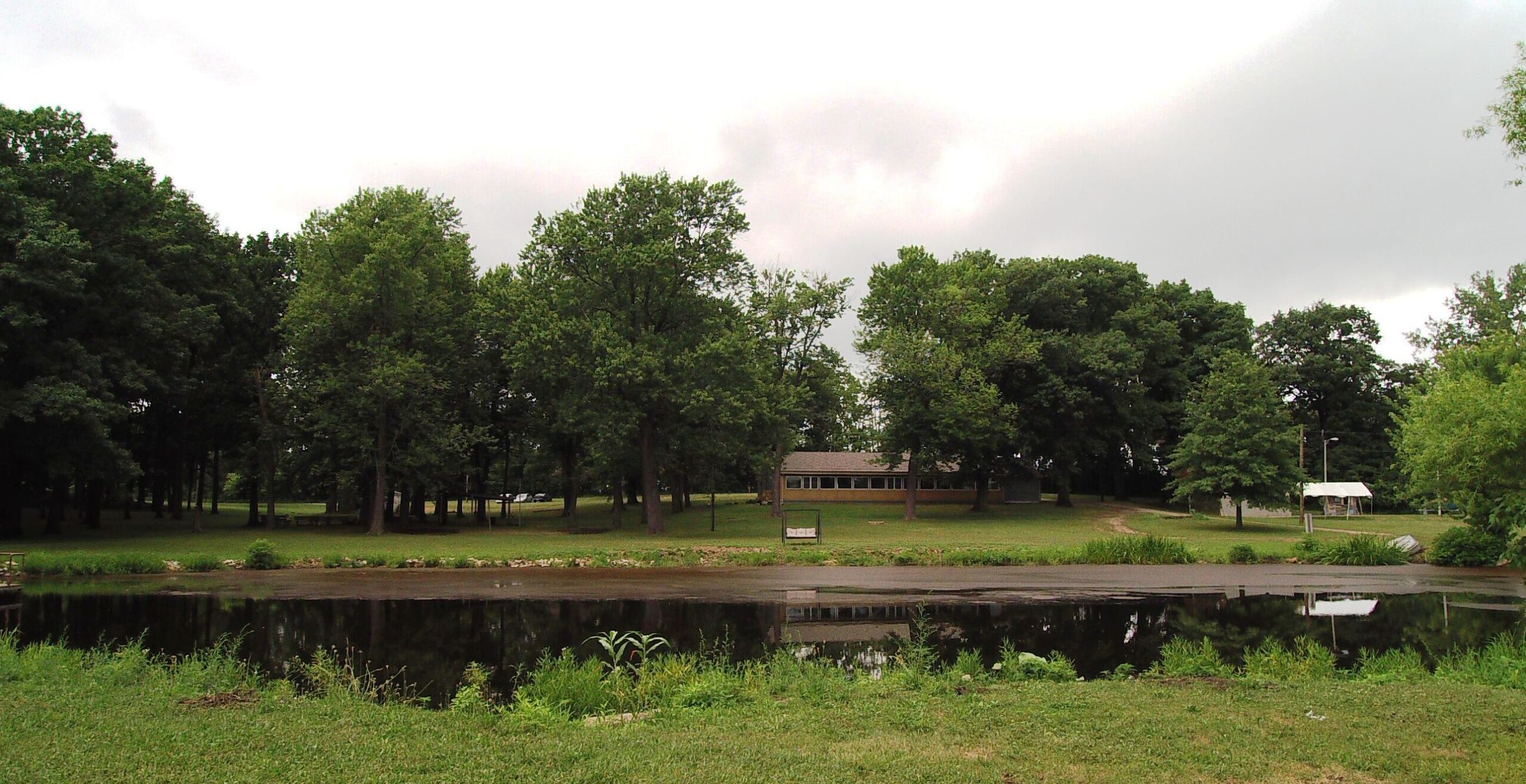 A peaceful park with a pond and trees under a cloudy sky.
