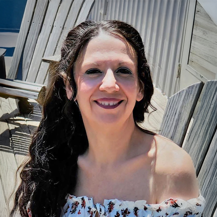 Smiling woman with long dark hair in a white off-shoulder top.