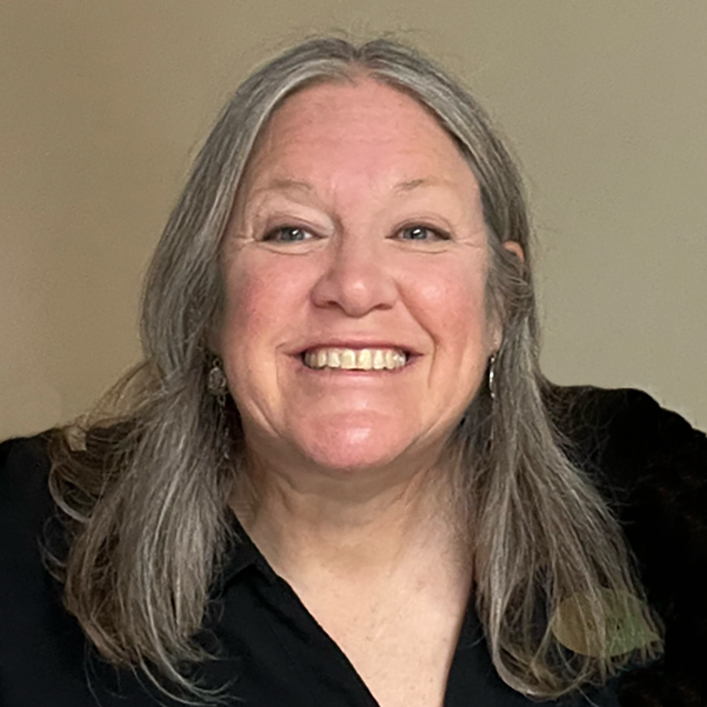 Smiling woman with long gray hair against a plain background.