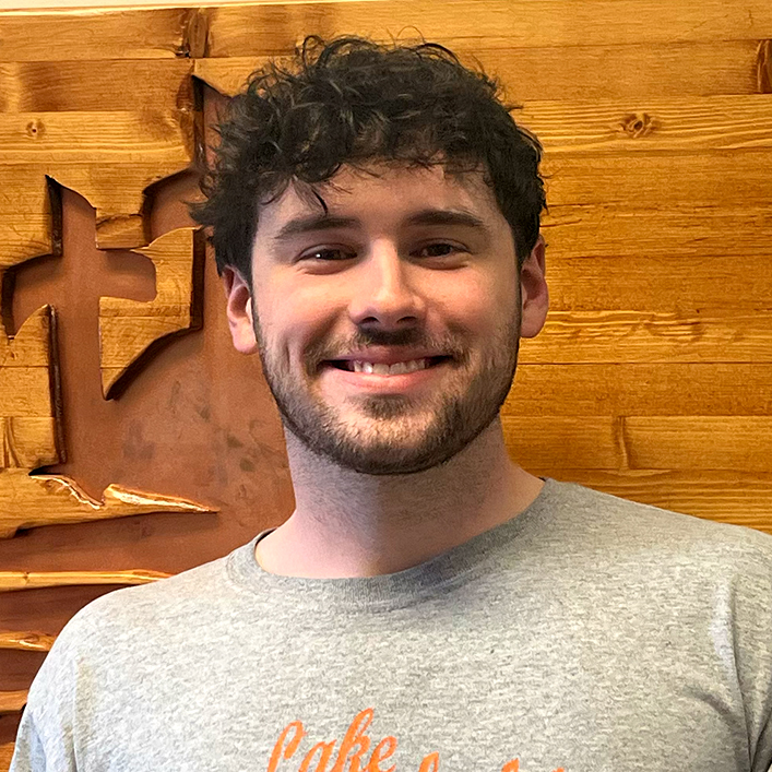 Smiling young man with curly hair in a casual gray shirt.