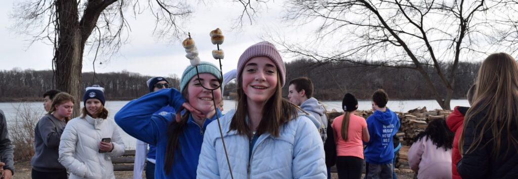 Two girls smiling outdoors, holding marshmallows on sticks.